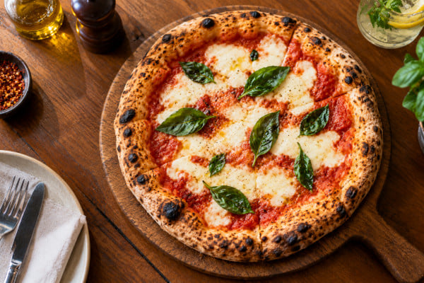 Close-up overhead shot of a freshly baked wood-fired margherita pizza on a rustic wooden board, melted mozzarella, fresh basil, casual restaurant setting