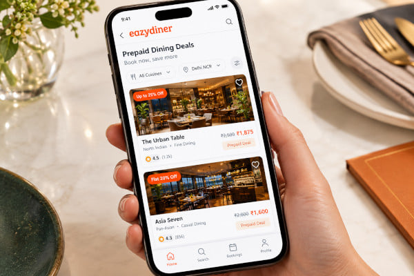 Close-up of a smartphone screen showing prepaid dining deal comparisons for two restaurants, with prices and cuisine labels visible, clean interface