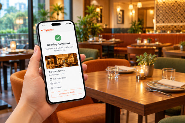 A smartphone showing a restaurant booking confirmation alongside a restaurant interior, warm tones, Indian urban dining setting